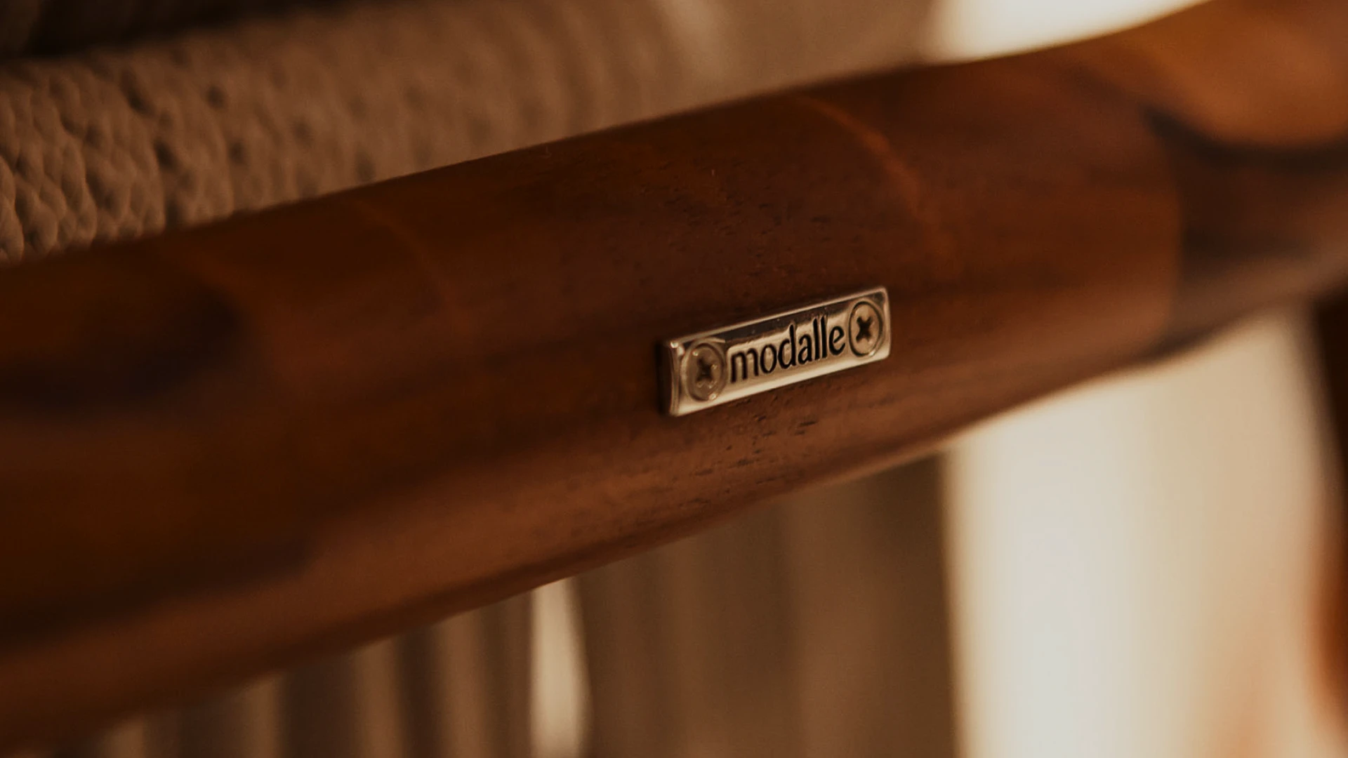 Detalhe de móvel Modalle com placa da marca aplicada em acabamento de madeira.