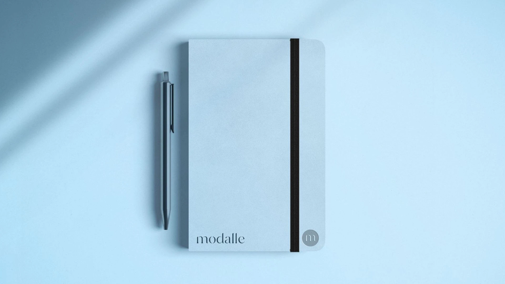 Caderno e caneta da Modalle com aplicação da identidade visual desenvolvida pela Toomorrow Branding.